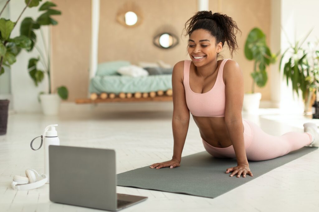 Happy african american woman stretching back and watching online tutorials on laptop, excercising in